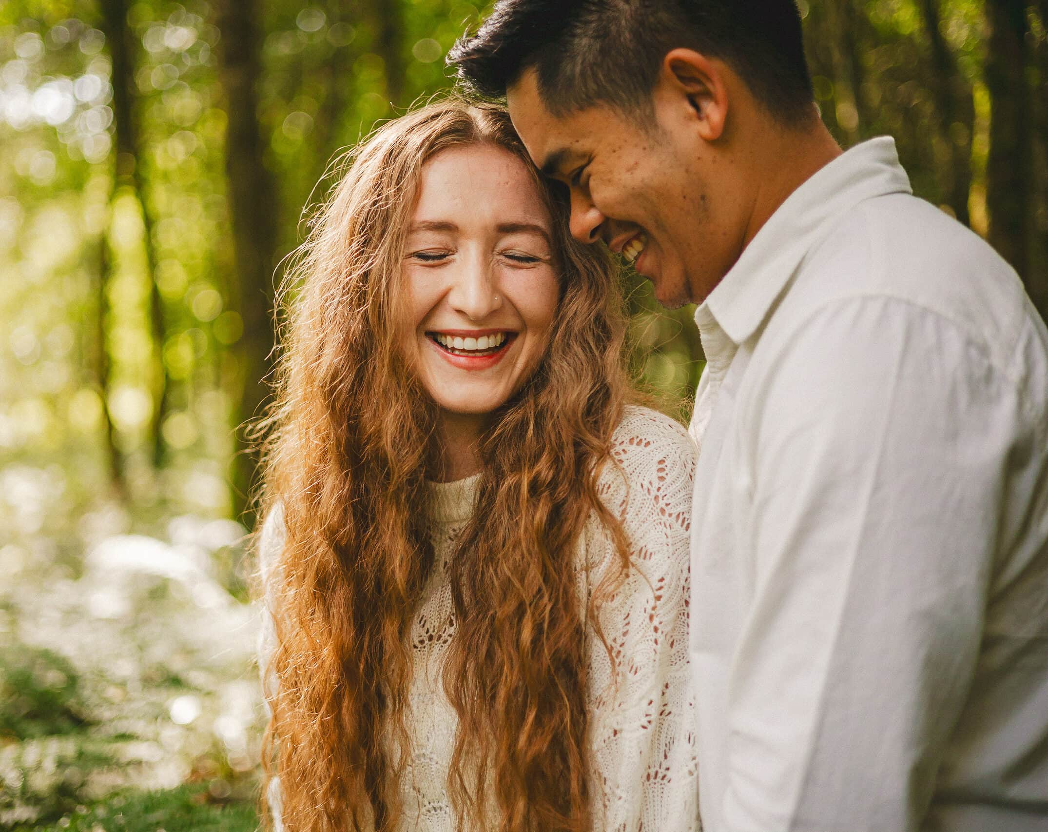 A couple shares laughter during their engagement session in the woods of Randalstown