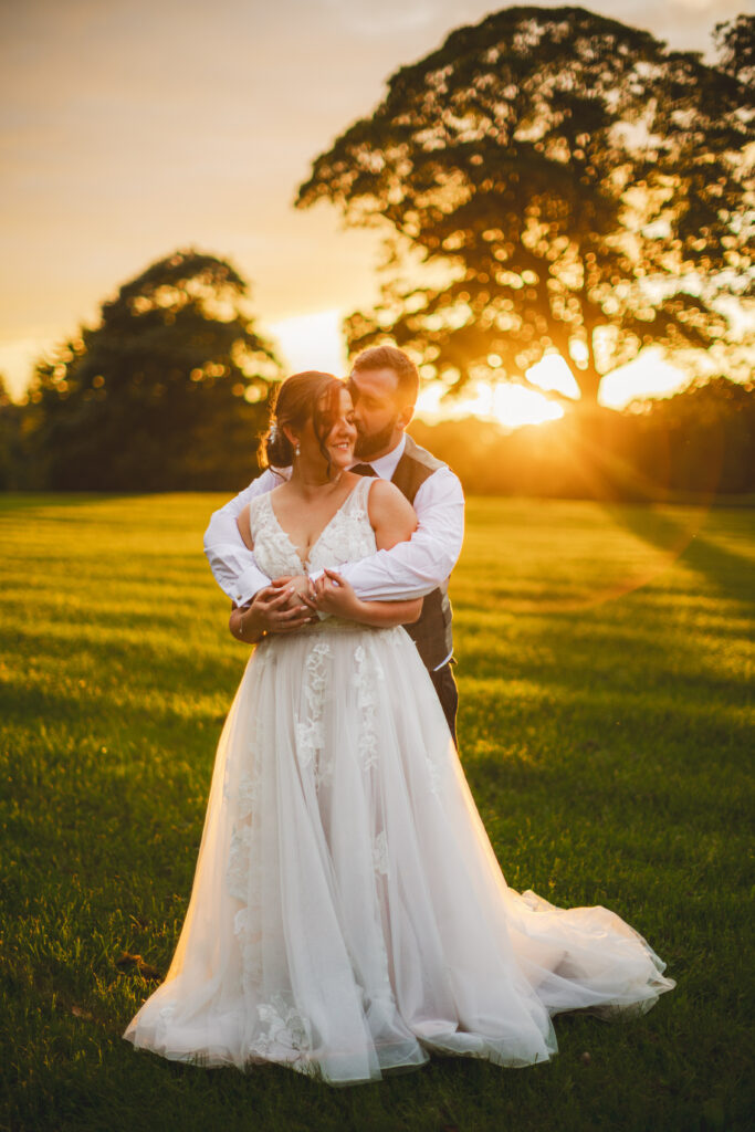 A bride and groom embrace in a field at sunset during their magical wedding at Drenagh Estate