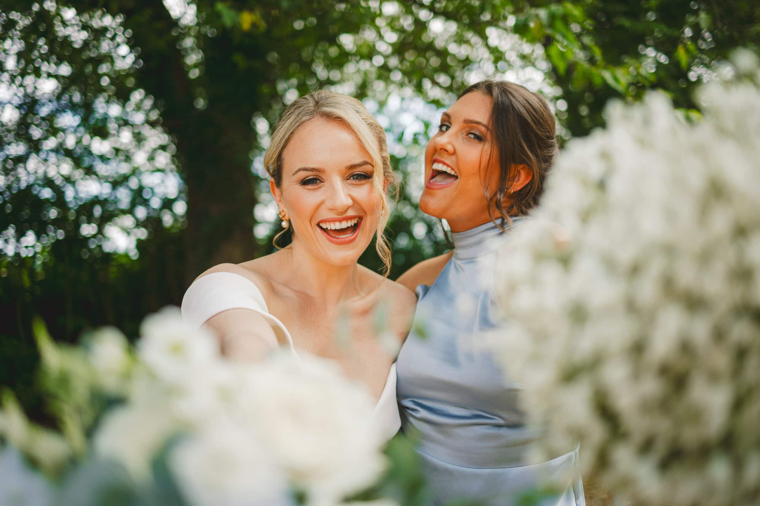 Two bridesmaids laughing while holding bouquets.