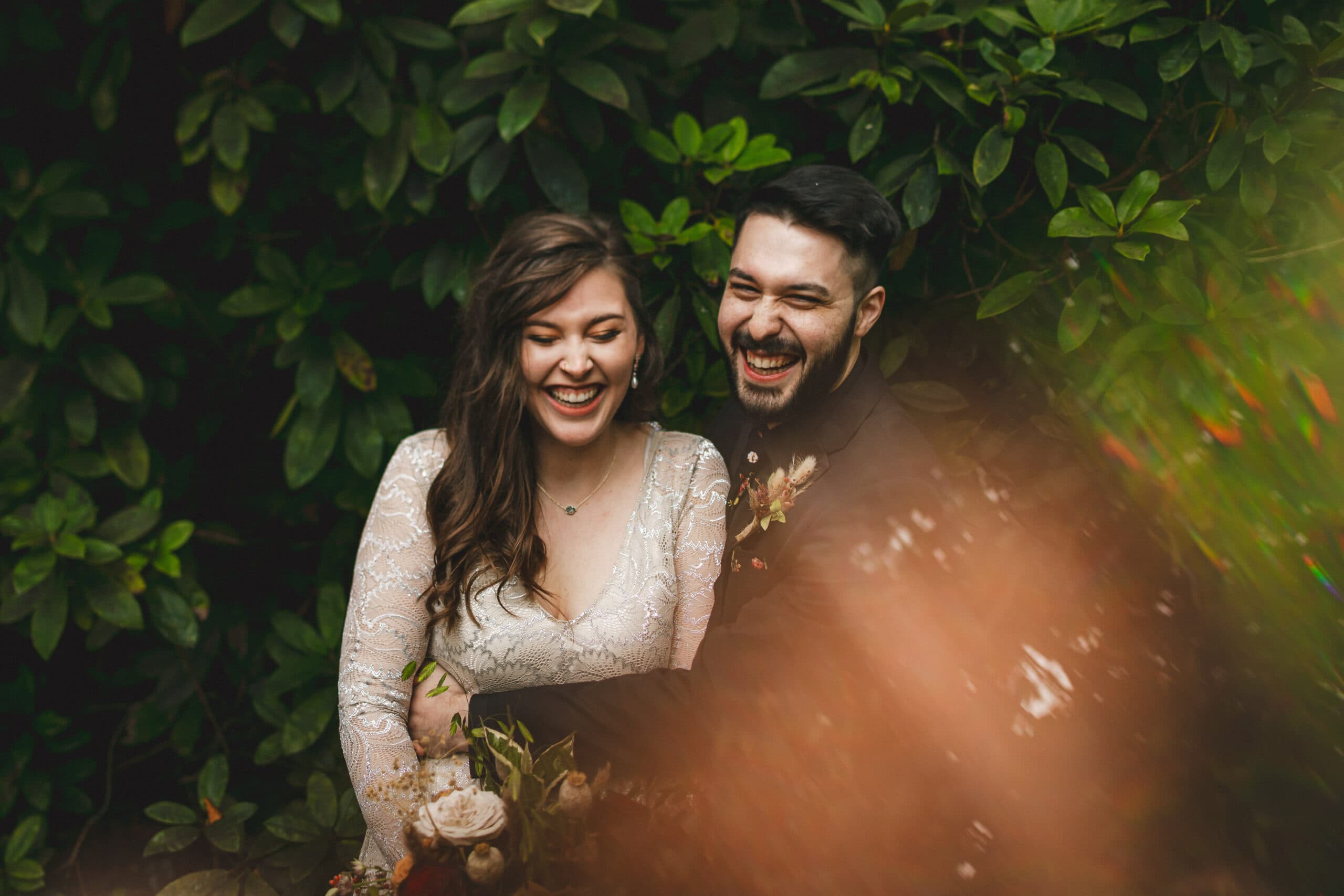 A happy bride and groom laughing in the woods surrounded by nature, creating a cozy and joyful atmosphere away from home.