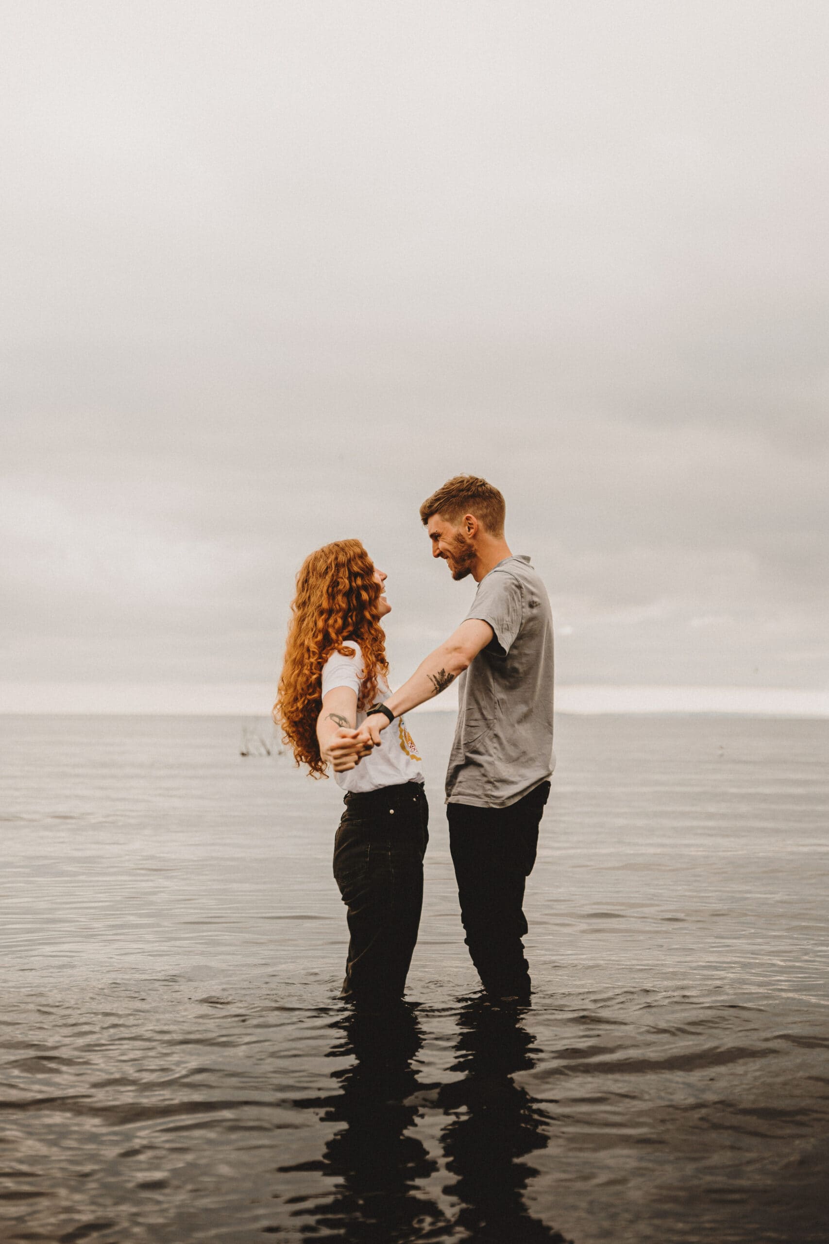 About: A couple standing in the water in front of a cloudy sky.