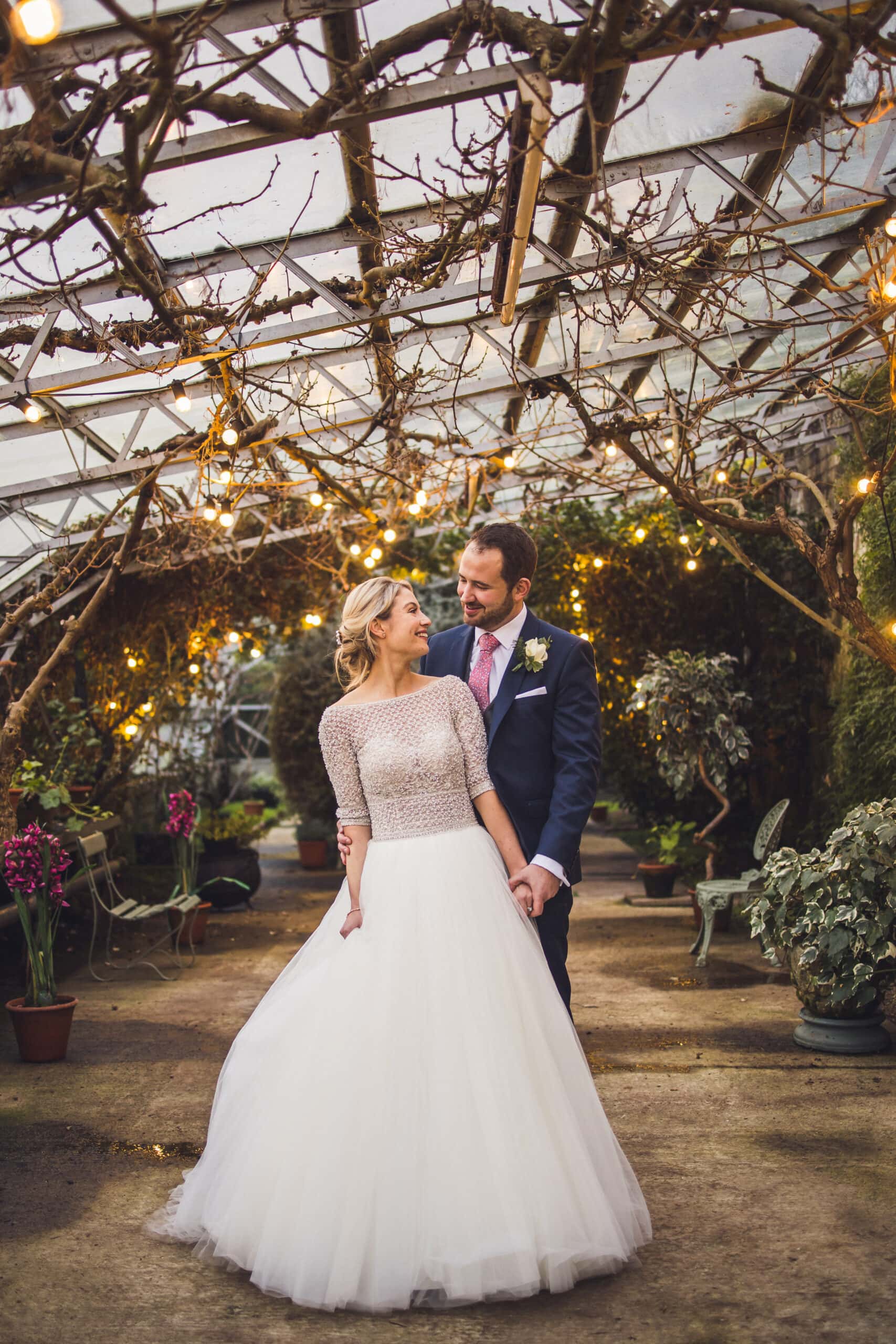 A stunning bride and groom glow amidst the enchanting lights of a magical greenhouse at Larchfield