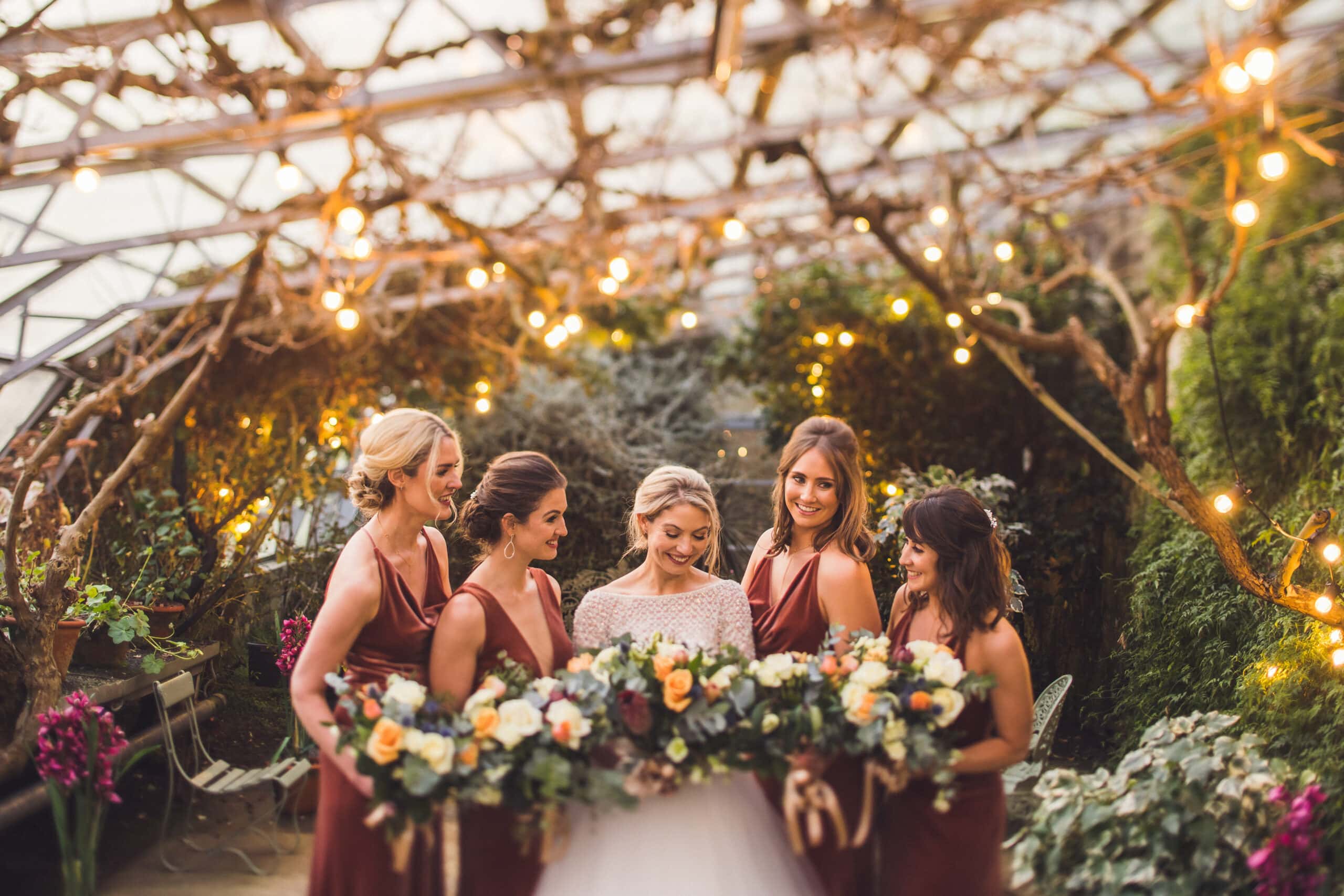 The bride and her bridesmaids pose in front of a greenhouse at Larchfield, one of the stunning Wedding Venues in Northern Ireland.