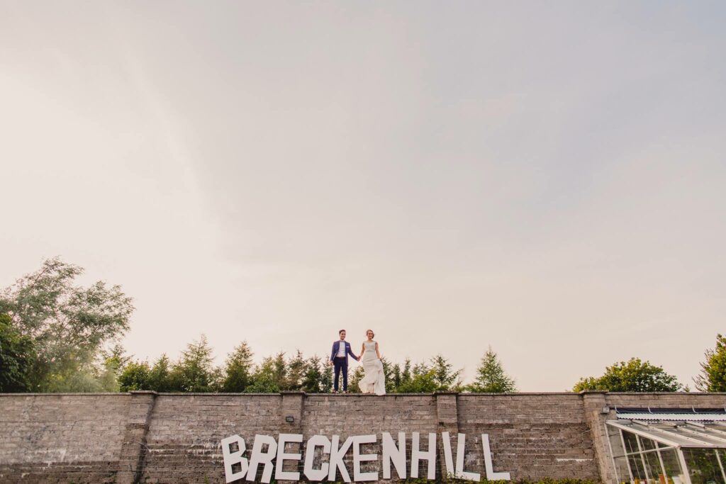 A bride and groom exchanging their vows at one of the stunning wedding venues in Northern Ireland, with a beautiful brick wall backdrop displaying the word Breckenhill.